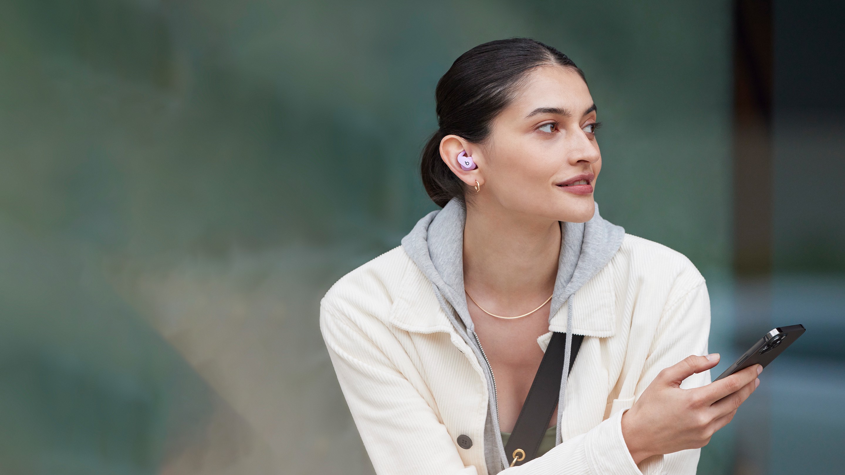 在户外佩戴 Beats Fit Pro 并手持 iPhone 的女性