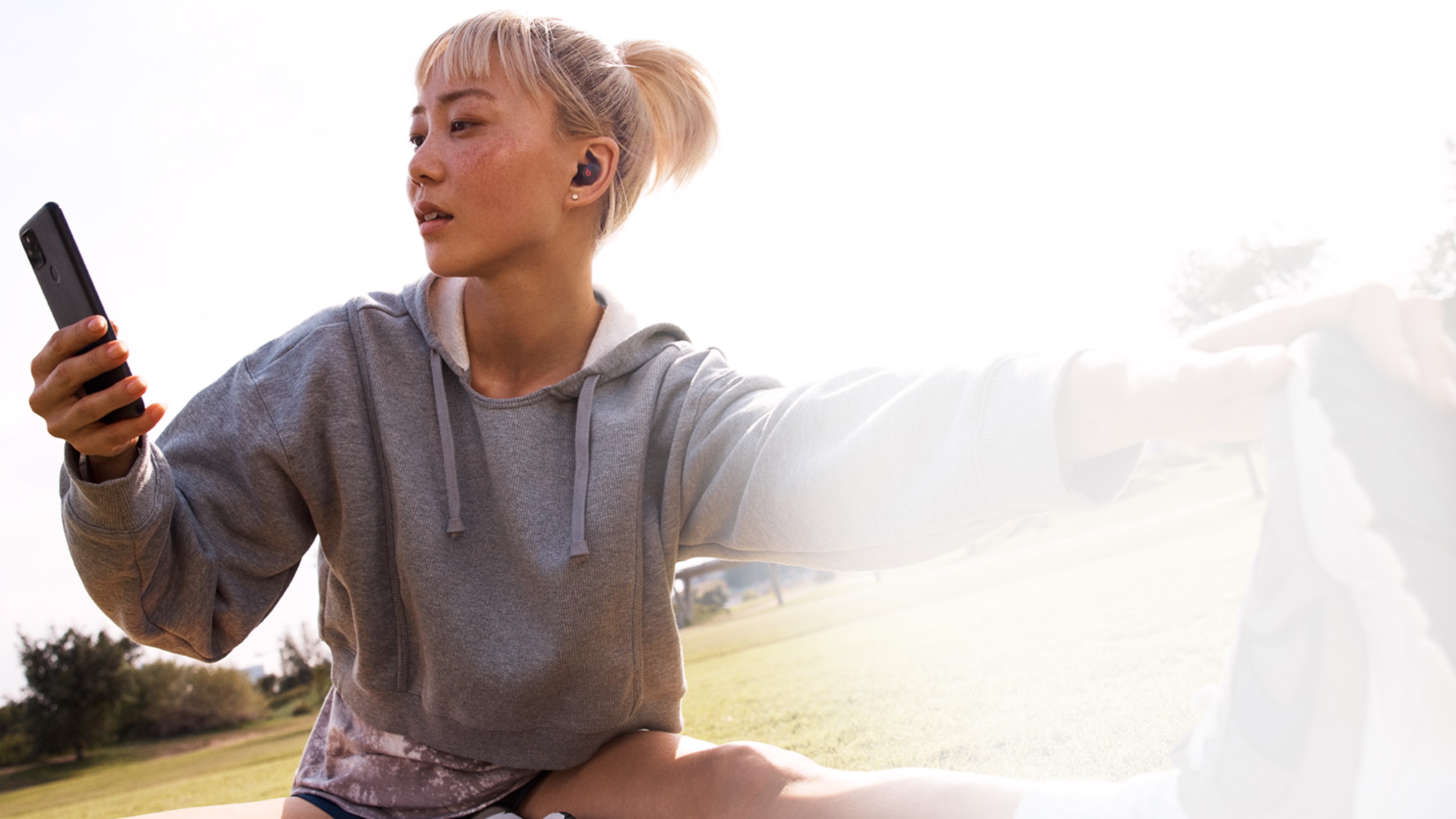 在户外进行伸展运动的女性佩戴 Beats Fit Pro 并使用 Android 设备